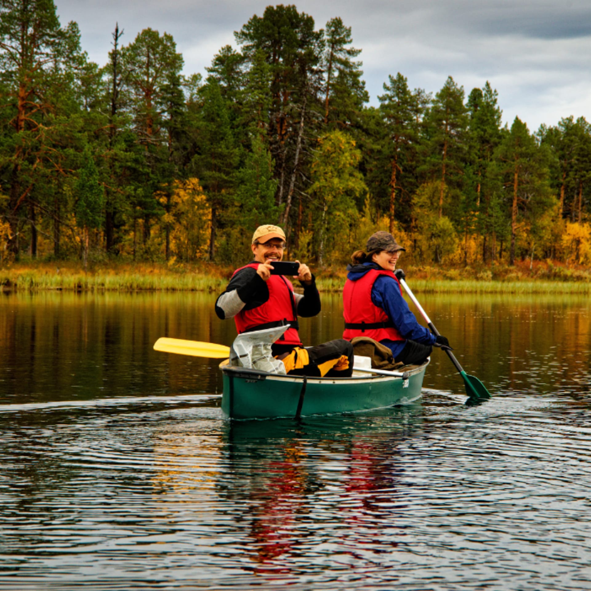 Two people are canoeing on a river in autumn.