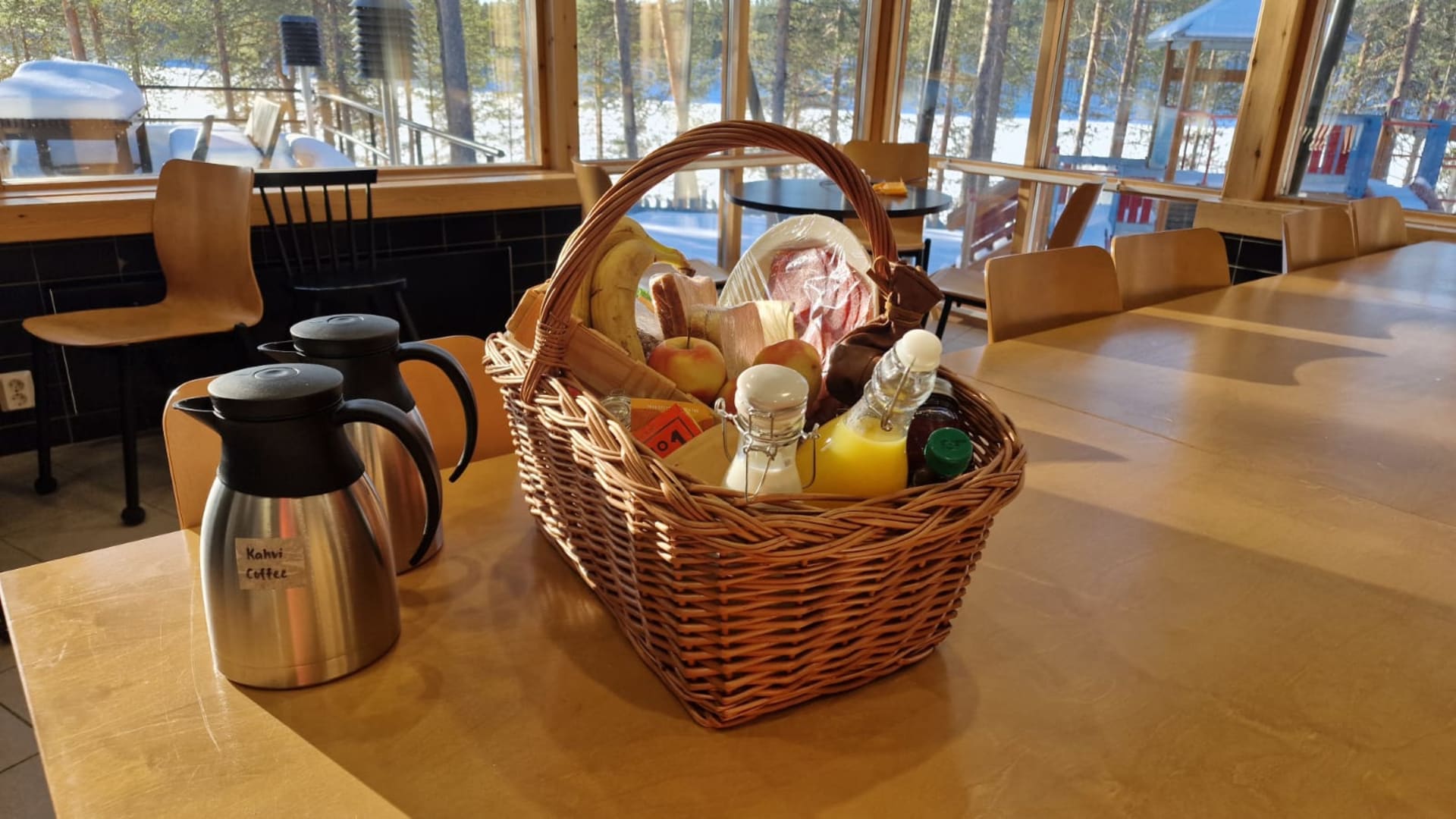 Aamiaskori ravintolan pyöydällä, korin vieressä termoskannuissa kahvia ja teetä.