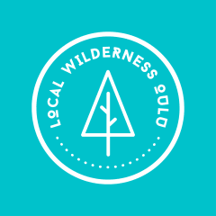Local Wilderness Oulu logo. White logo on blue background. A circle that has a tree in it and the text Local Wilderness Oulu.