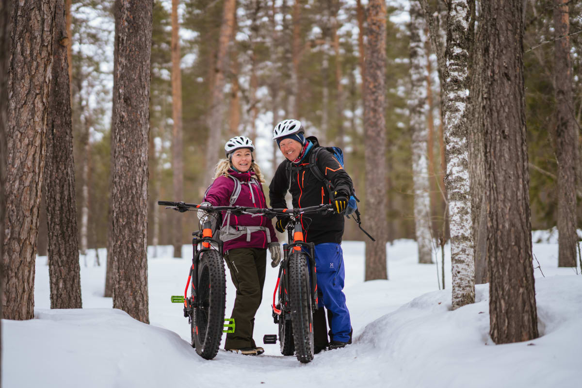 Kaksi hymyilevää pyöräilijää talvisessa metsässä Pyhä-Luoston kansallispuistossa. Kuva: Jaakko Posti