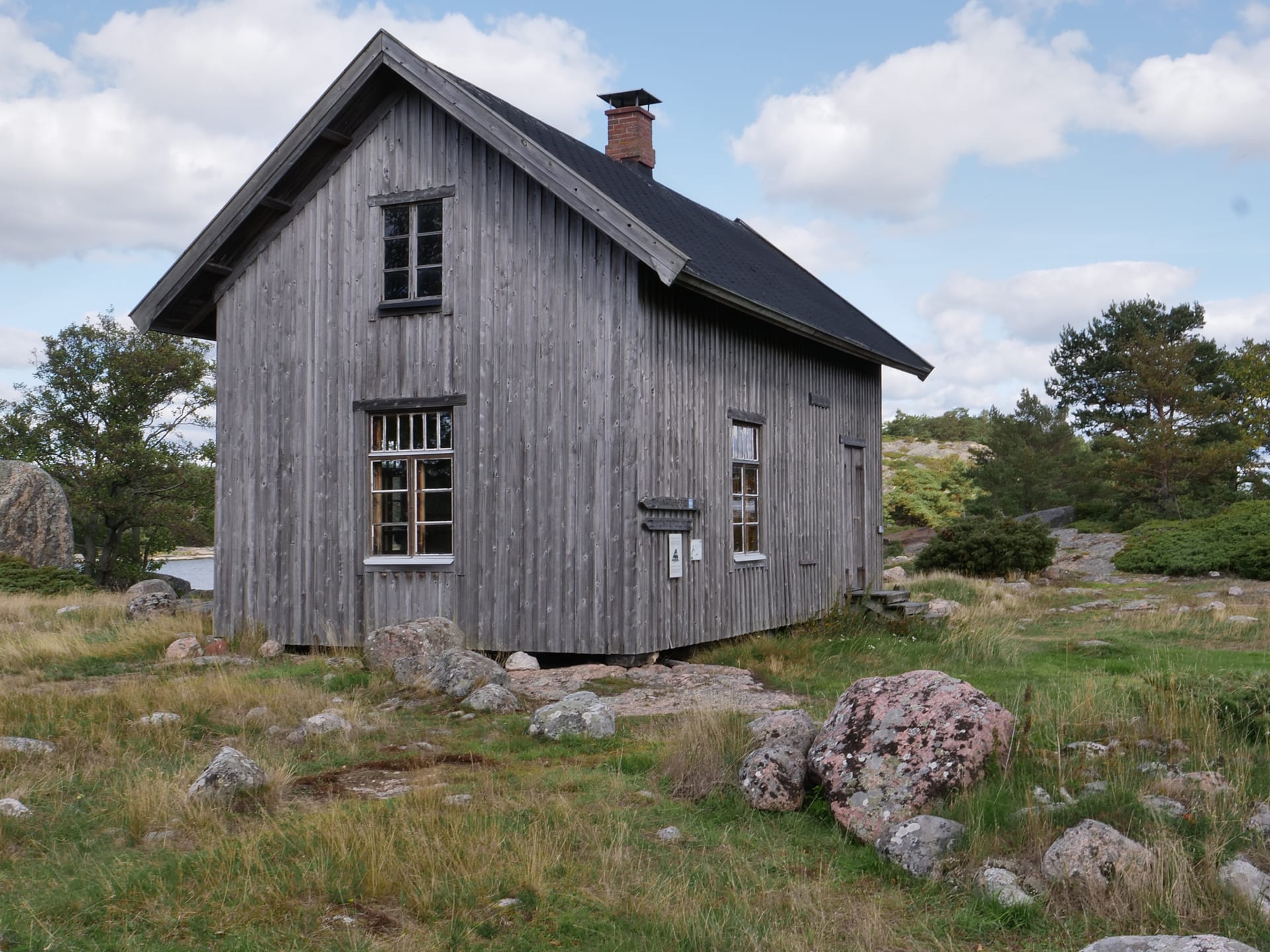 Harmaa, lautarakenteinen rakennus.  En grå brädinramad byggnad.  A gray board-framed building.