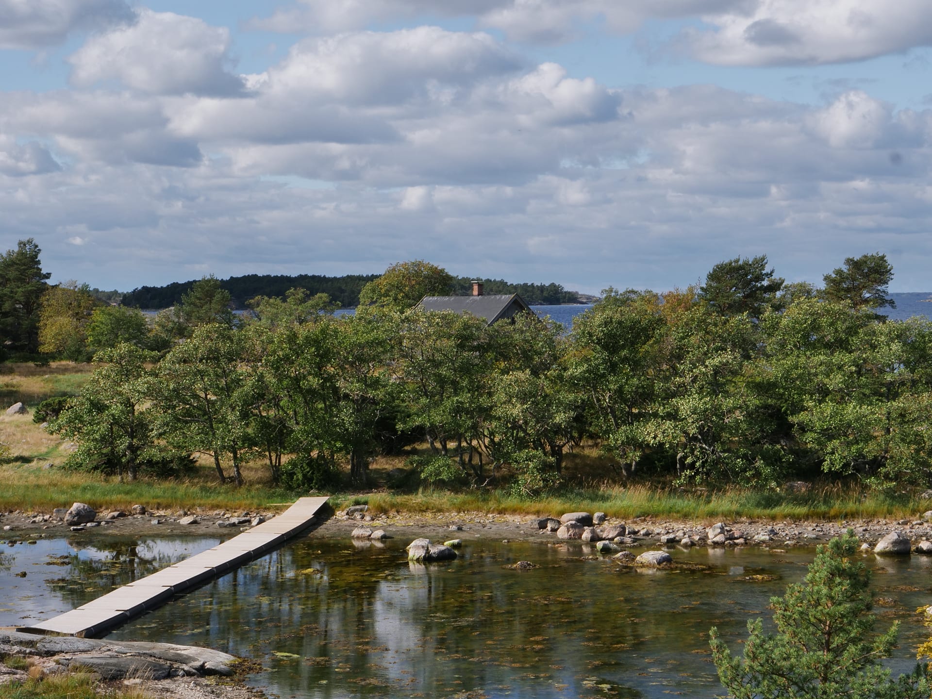 Vasemmalla reunalla näkyy seuraavalle saarelle vievä ponttonisilta. Saaren puuston yli pilkottaa talon katto.The picture is taken from a high rock down. On the left side you can see the pontoon bridge leading to the next island  Vasemmalla reunalla näkyy seuraavalle saarelle vievä ponttonisilta. Saaren puuston yli pilkottaa talon katto.The picture is taken from a high rock down. On the left side you can see the pontoon bridge leading to the next island
