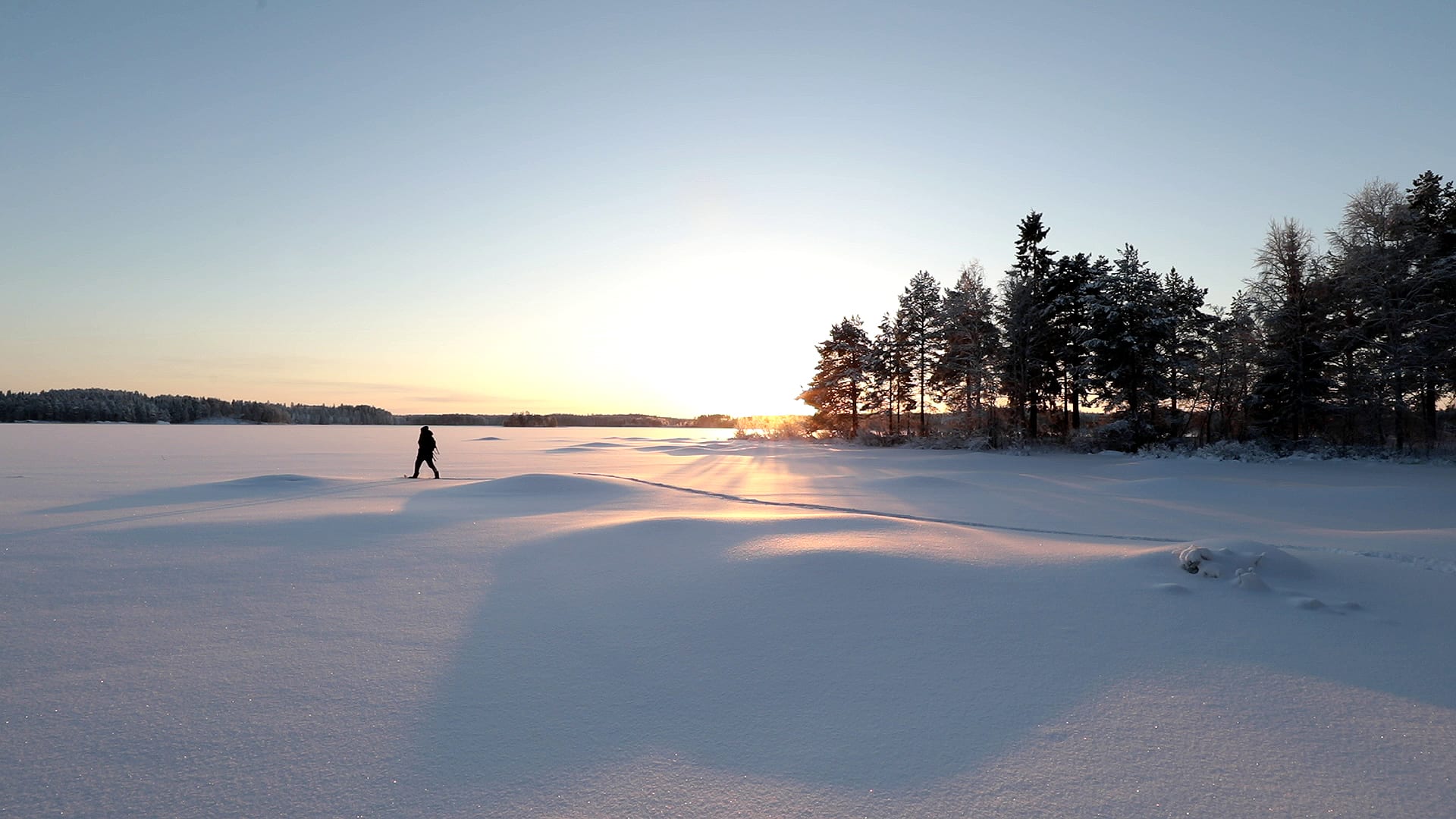 A snowshoe adventurer heads from Villa Cone Beach lakefront onto the untouched snowy lake ice with the noon sun just over the horizon.