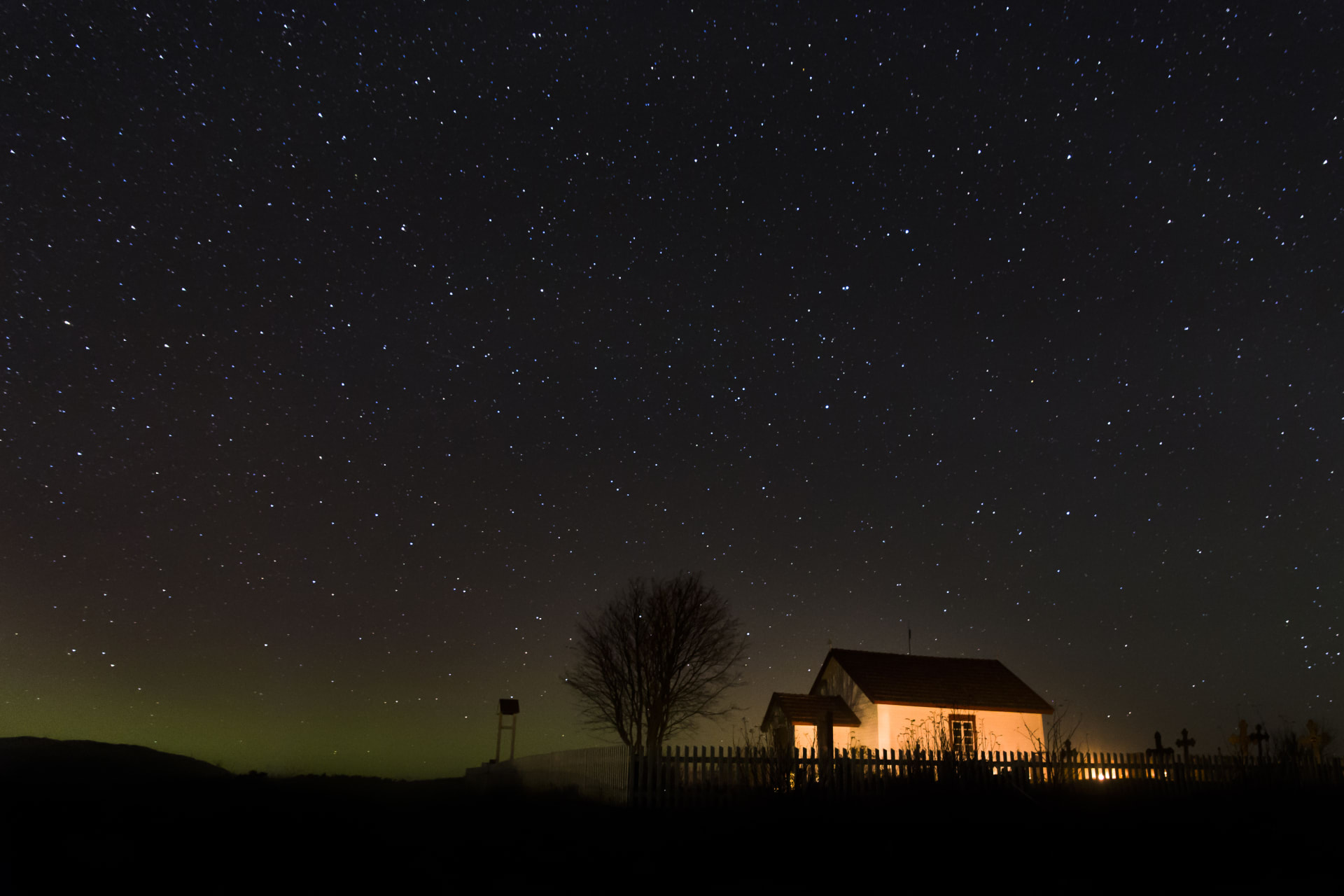 On yö ja taivaalla on tähtiä. Kuvan oikeassa reunassa on valaistu kappeli.   It is night and there are stars in the sky. On the right side of the picture is an illuminated chapel.