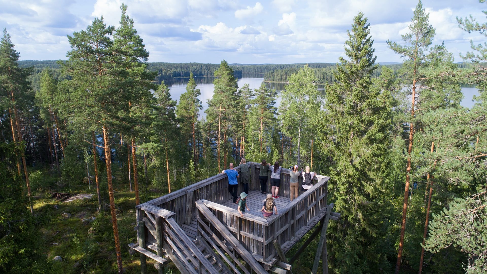 People watching the lake scenery from a scenic tower in a forest.