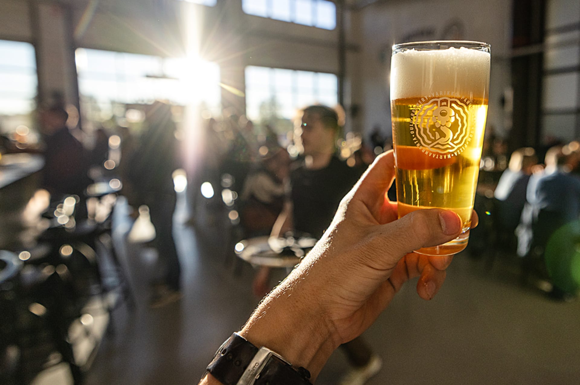 Close-up of a hand holding a fresh, frothy local craft beer with a warm lens flare
