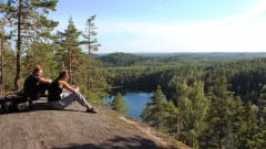 Two women admiring the view from a big rock high up from a lake