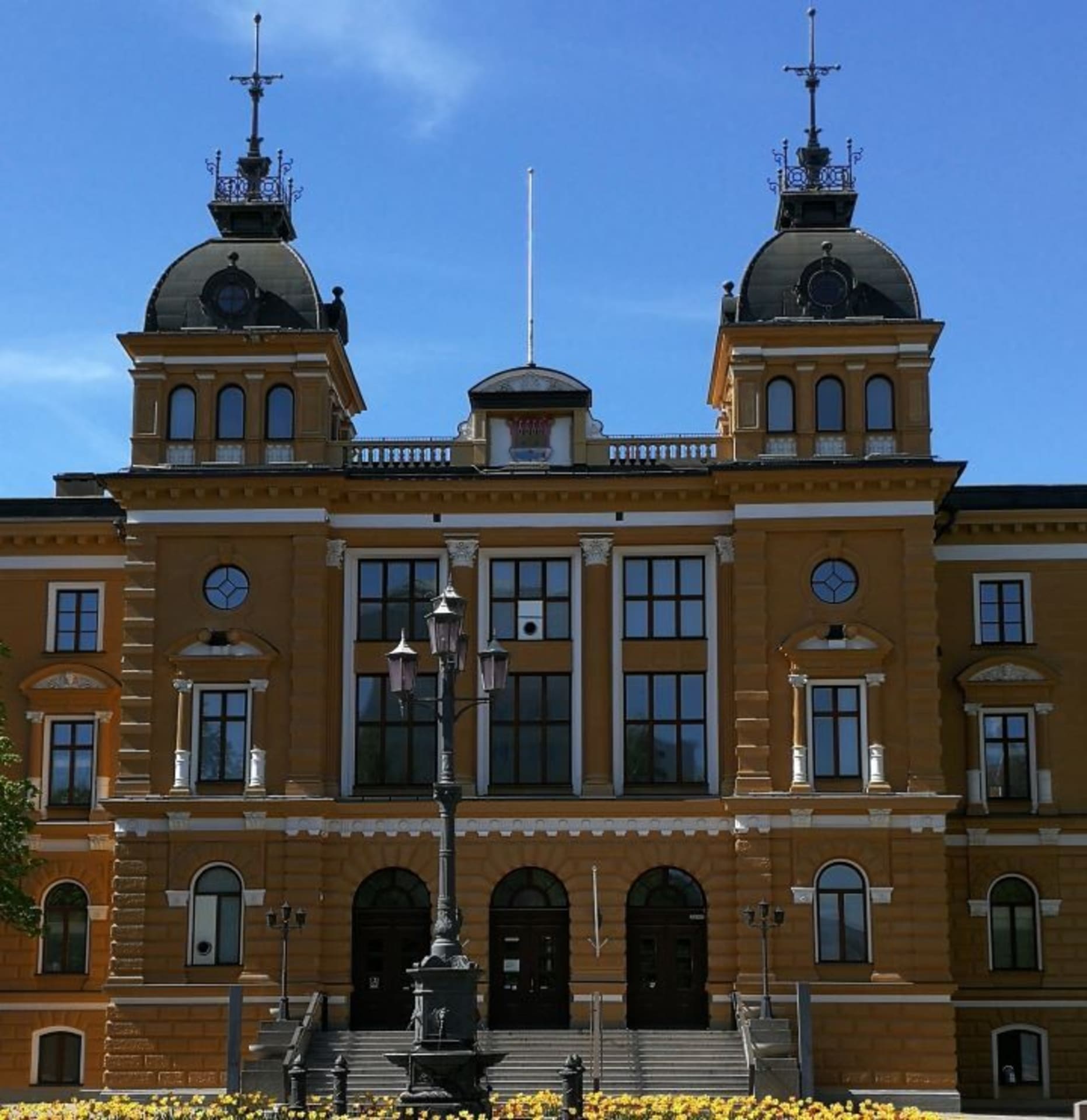 Brownish Oulu city hall with three main doors and two little towers. Background blue sky.
