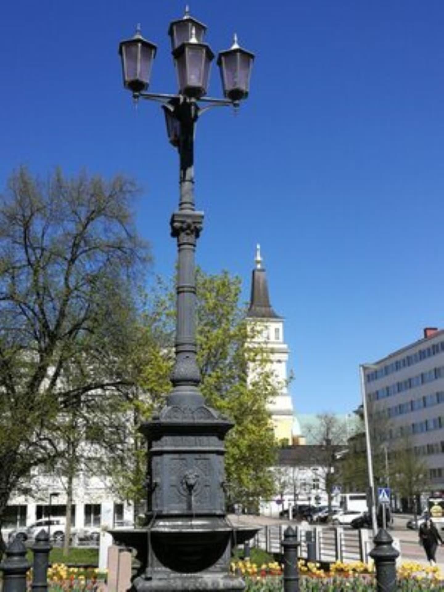 Scottish fountain in front of Oulu City Hall in summer. Background Oulu Cathedral and clear blue sky.