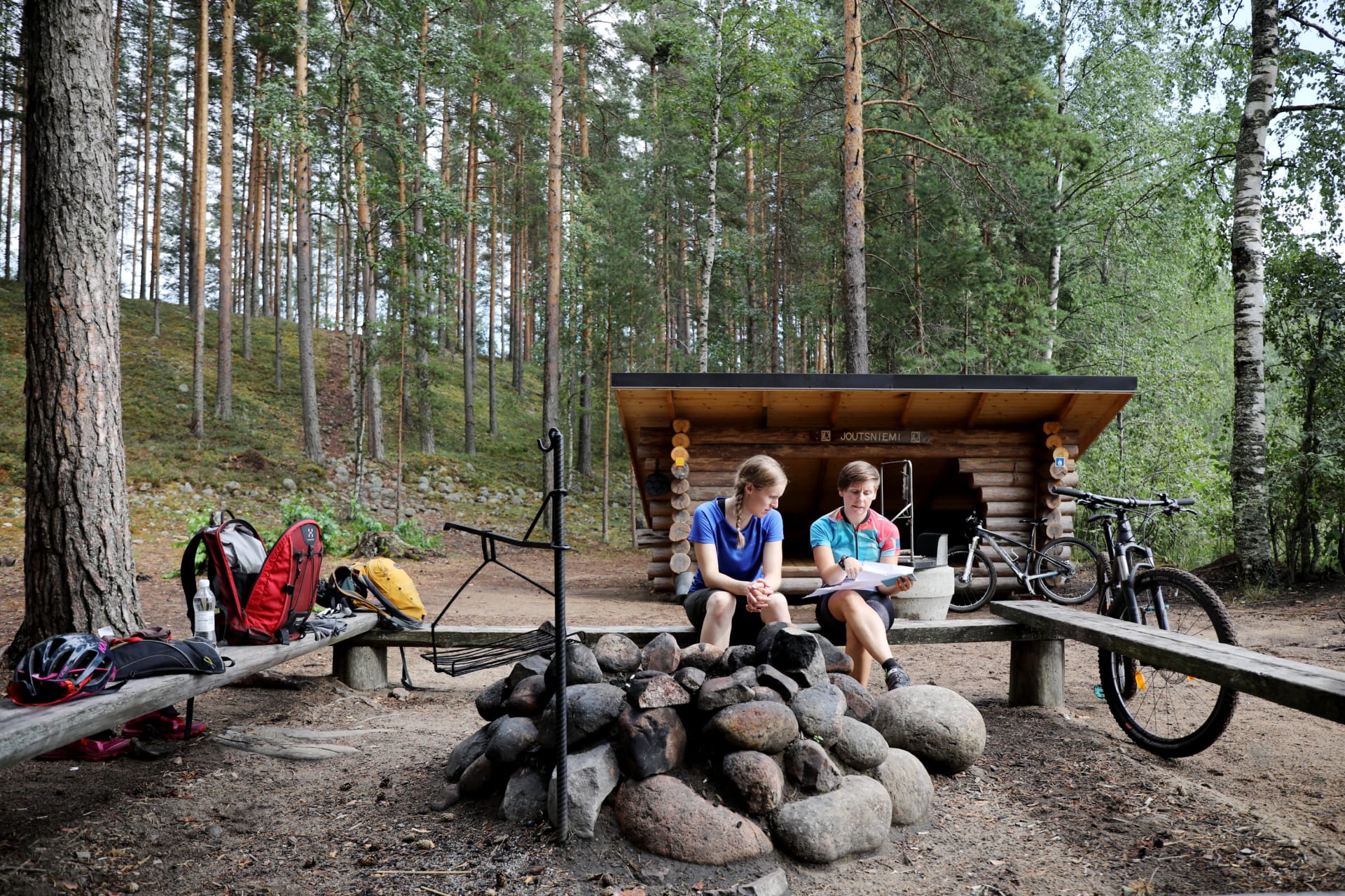Retkeilijöitä nuotiopaikalla kesäisessä Leivonmäen kansallispuistossa. Taustalla laavu ja metsää. Kuva: Touho Häkkinen