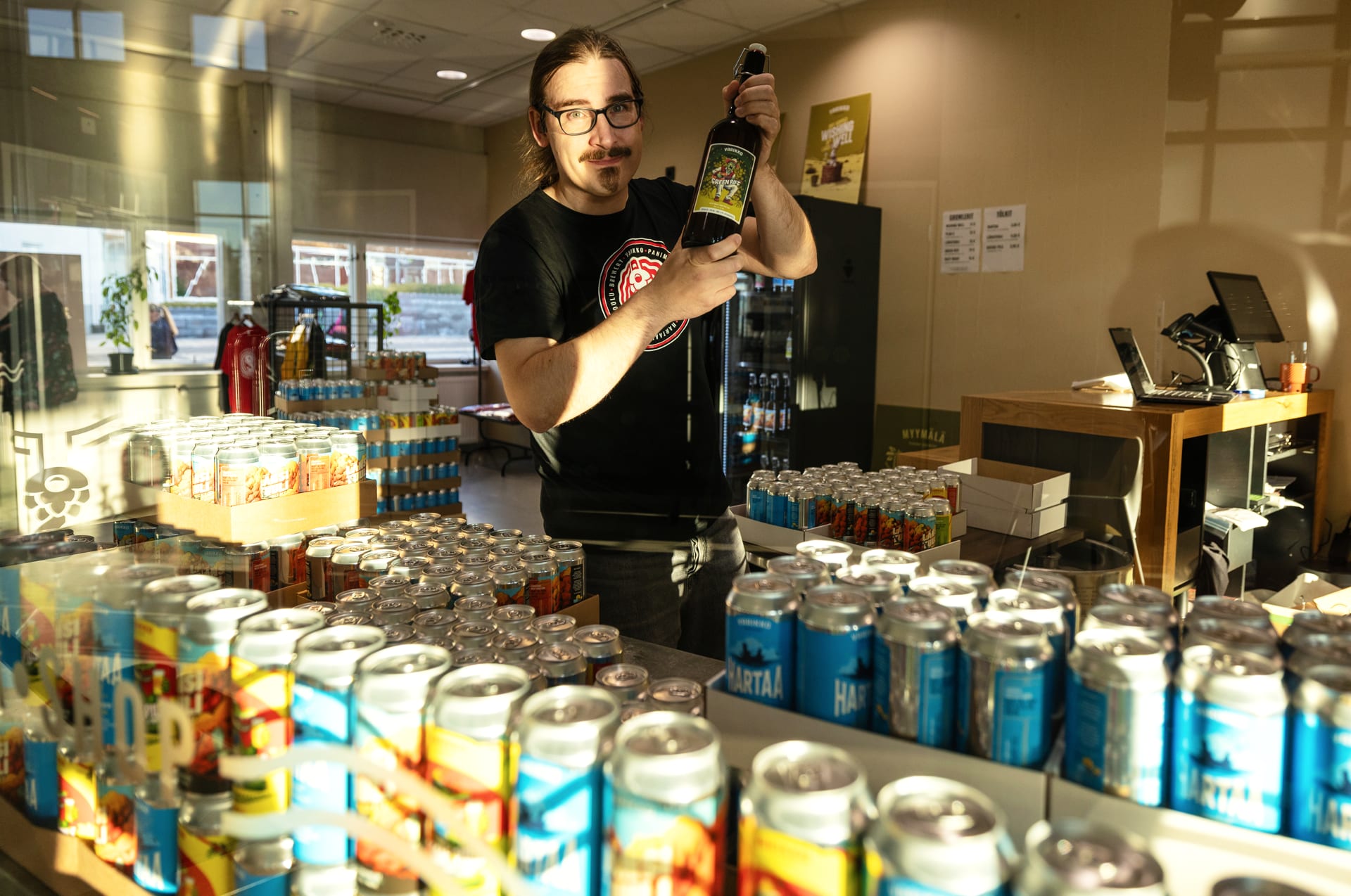 Friendly Varikko staff member offering fresh growlers and cans directly behind the shop counter