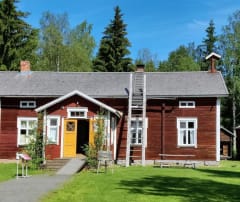 The old red wooden building with yellow doors in Turkansaari in midsummer. Two birch trees located both sides of the yellow doors to celebrate midsummer. Foreground green grass.