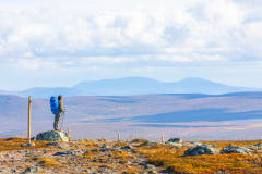 Retkeilijä seisoo kivellä tunturin laella syksyisessä Pallas-Yllästunturin kansallispuistossa. Taustalla avotunturimaisema ja tunturijono. Kuva: Rami Valonen