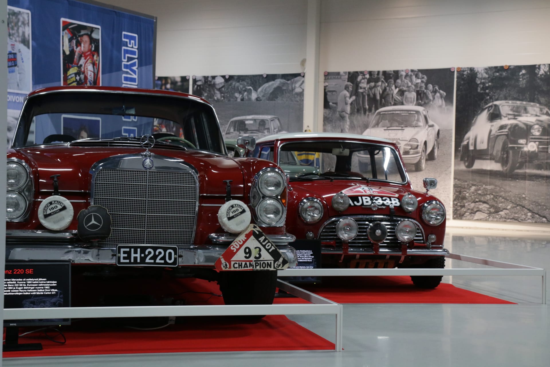 Kaksi punaista, vanhaa ralliautoa. Vasemmalla iso Mercedes-Benz ja oikealla pieni Mini.