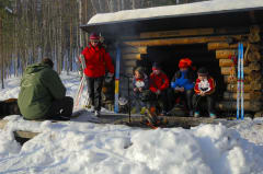Joukko retkeilijöitä viettämässä taukoa kevättalvisella laavulla. Kuva: Heikki Räsänen