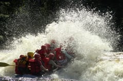 Koskelaskua kumiveneellä. Veneen kyydissä joukko retkeilijöitä. Koski kuohuu ja vesi pärskyy kesäpäivänä. Kuva: Heikki Räsänen