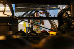 Tyttö kurkistaa kameraan veturin alapohjan välistä.