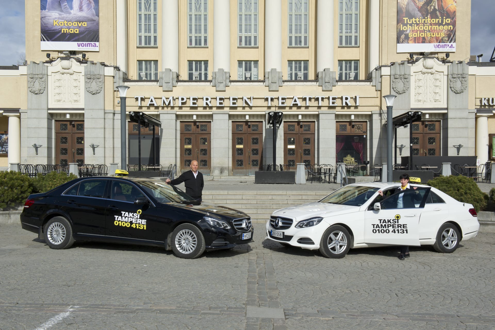 In front of Tampere Theatre, two taxis are parked, with a male driver and a female driver standing happily next to them.