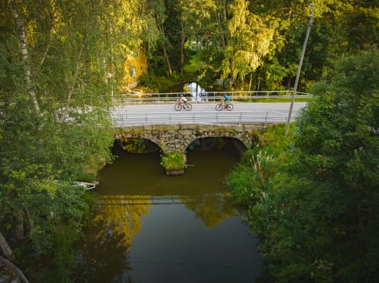 Aerial view of a couple cycling on the stone bridge over the water in Urjalankylä Village in summer.