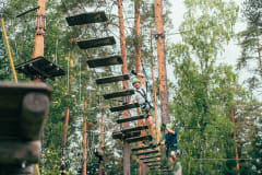 Mies kävelee puiden väliin vaijereilla kiinnitettyjä lautoja pitkin kohti toista puuta. Pajulahti Seikkailupuisto
