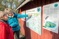 Kaksi retkeilijää tutkii lautaseinäisen vajan seinällä olevaa Saaristomeren kansallispuiston karttaa. Kuva: Martti Komulainen.