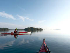 Aurinkoa, tyyni meri, toinen meloja siirtyy vasemmalta oikealle, kuva otettu taaempana tulevasta kajakista. Kuva: Sanna-Mari Kunttu.