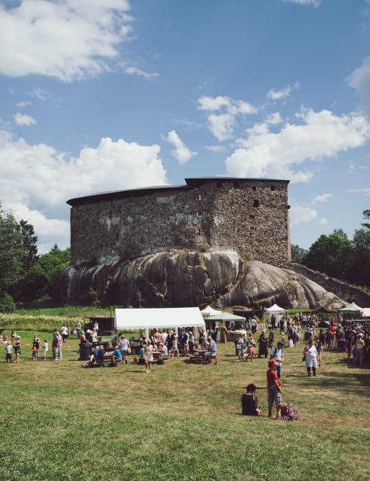 Rauniolinnan pihalla ihmisiä ja kojuja Keskiaika -tapahtumassa. Taustalla Rauniolinna. Kuva:Multifoto