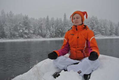 Woman sitting on snow in meditation with eyes closed.