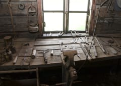 In the picture, there is a table inside a blacksmith’s workshop. On the table, there are various tools.