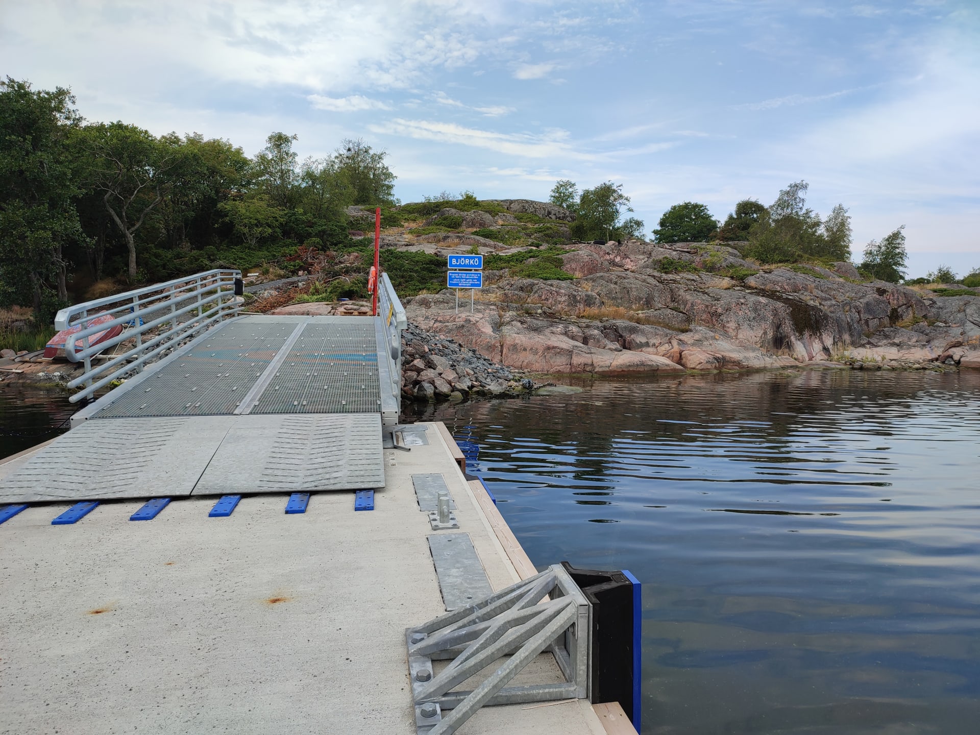 Kuva yhteysaluslaiturilta rannalle päin. Kalliolla on kyltti, jossa lukee saaren nimi.Picture from the connecting pier facing the beach. There is a sign on the rock that says the name of the island. 