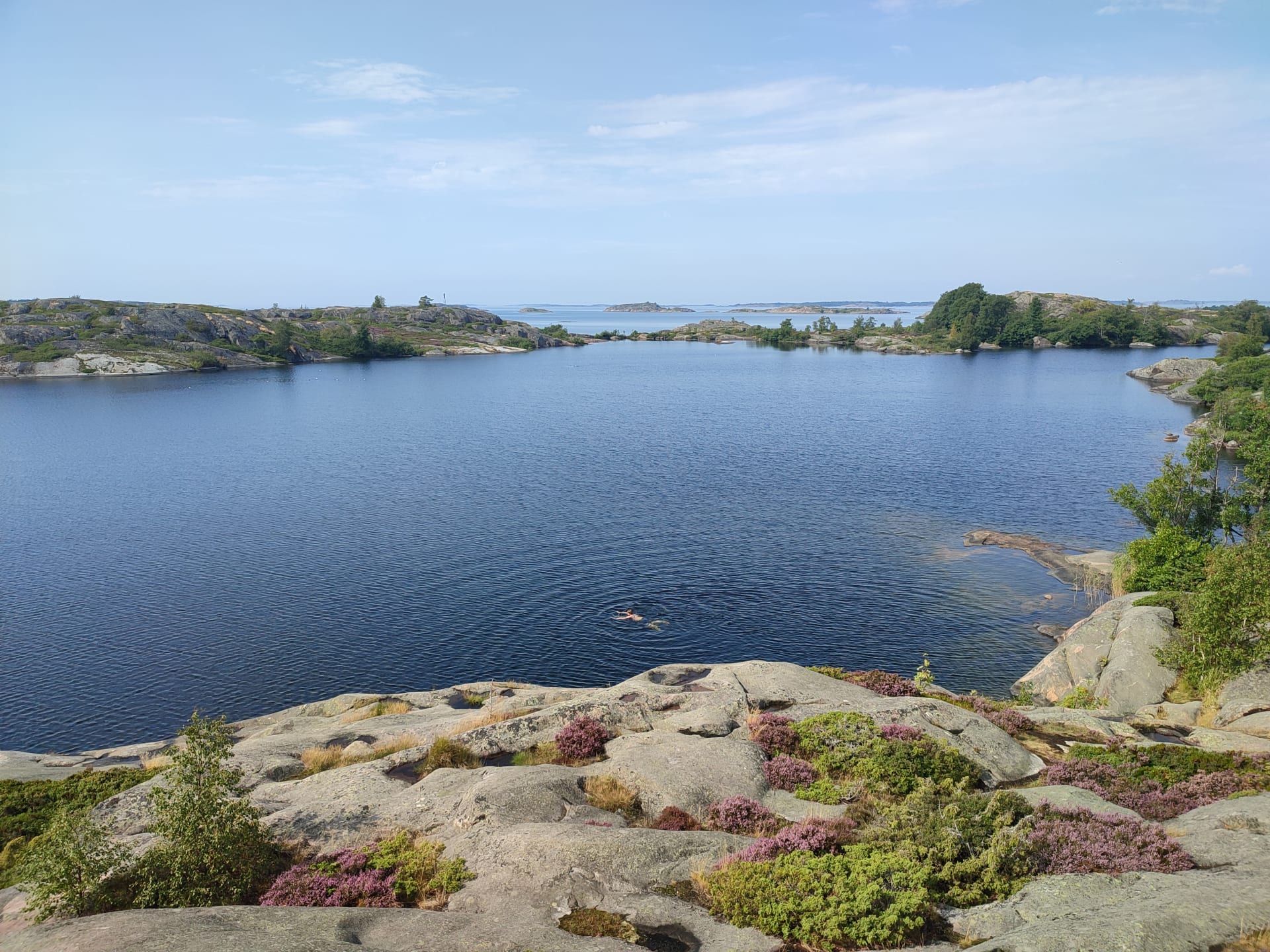 Sisäjärvessä ui ihminen. Järveä kehystää kalliot. Kallioiden takaa näkyy merta.A person swims in the inner lake. The lake is surrounded by rocks. You can see the sea behind the rocks.