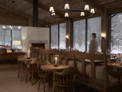 An intimate dining area at Jänkä Resort with wooden chairs, candlelit tables, and warm lighting, creating a calm evening atmosphere beside snowy forest views.