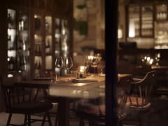 A close-up view of a candlelit restaurant table at Jänkä Resort with wine glasses, wooden furniture, and warm reflections, creating an intimate dining mood.