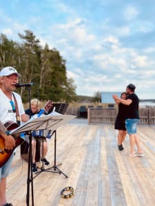 A musician performs live, creating a vibrant backdrop for a couple dancing on the deck, all set against the laid-back ambiance of an archipelago setting.