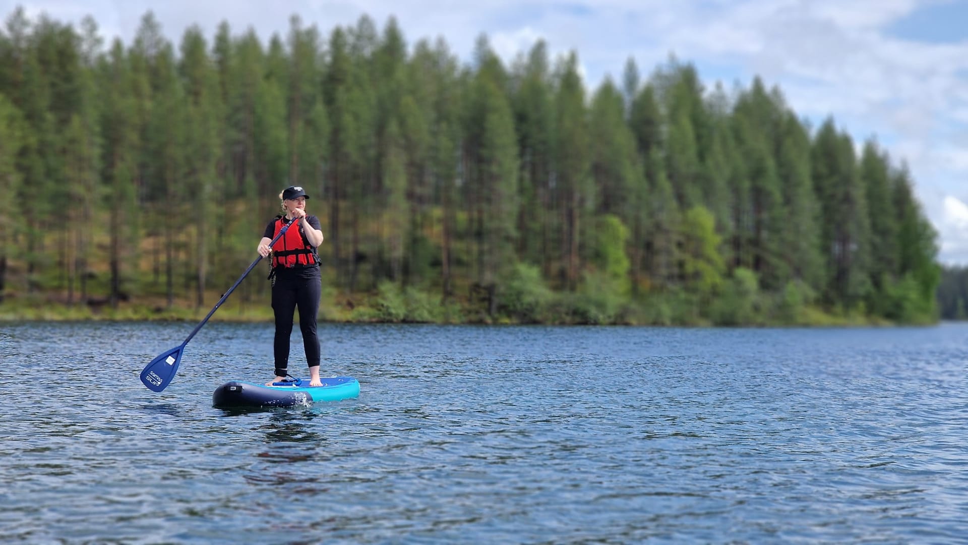 Nainen seisoo Sup-laudan päällä ja meloo Öllöri-järvellä Hossassa