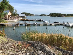 A picturesque dock with moored boats, a rustic building in the background, and lush greenery captures the essence of tranquility in the archipelago.