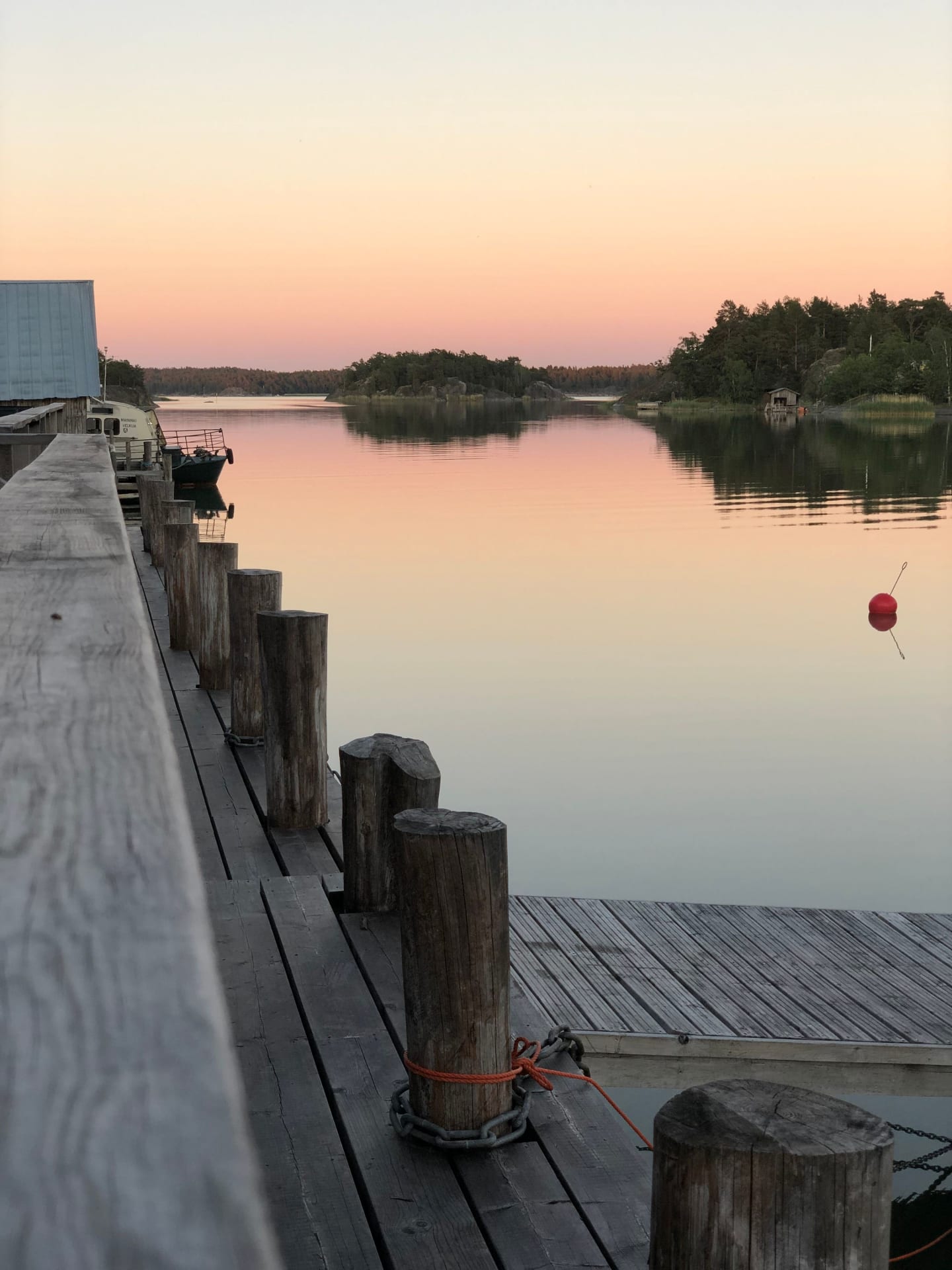 The gentle hues of dawn or dusk reflect on the calm waters seen from the wooden jetty, promising stillness and natural beauty in the archipelago.