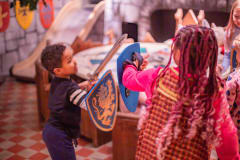 Two children are playfighting with soft swords in the room of King Arthur and his Knights.