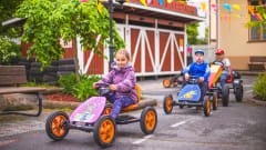 Children are driving with pedal cars in the Fun on wheels Yard.