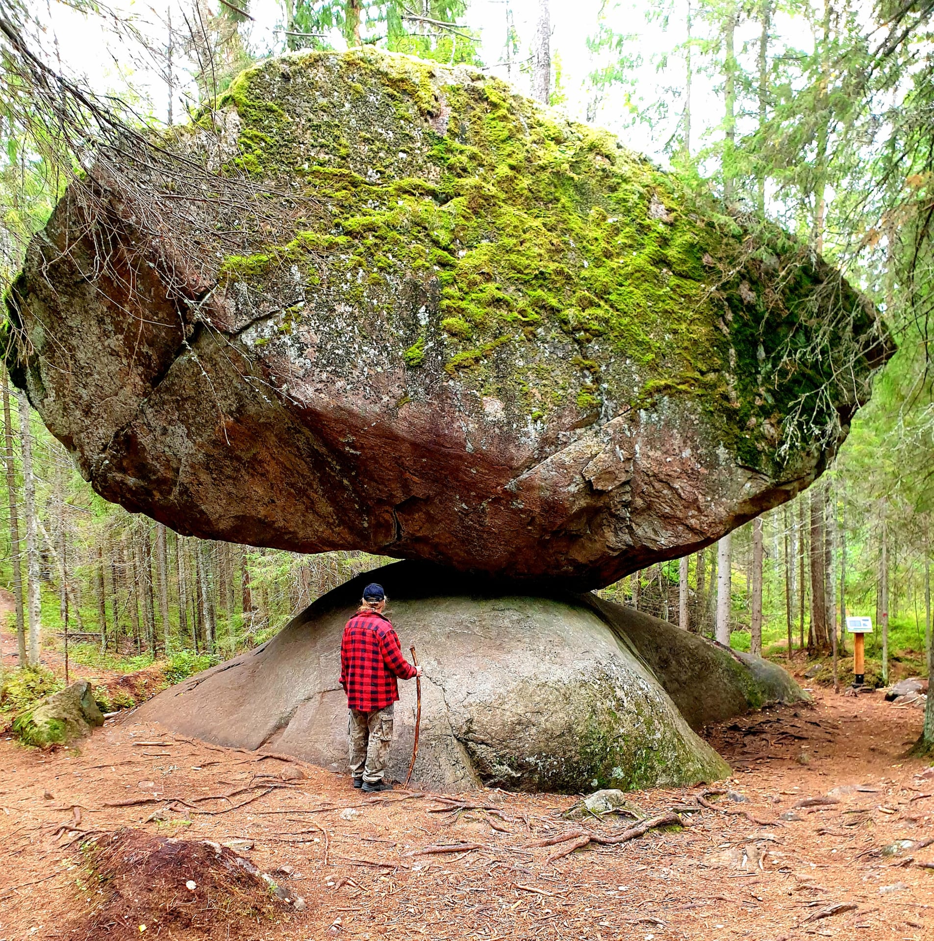 Ihminen seisoo Kummakiven vieressä.  Kivi tasapainoilee silokallion päällä.