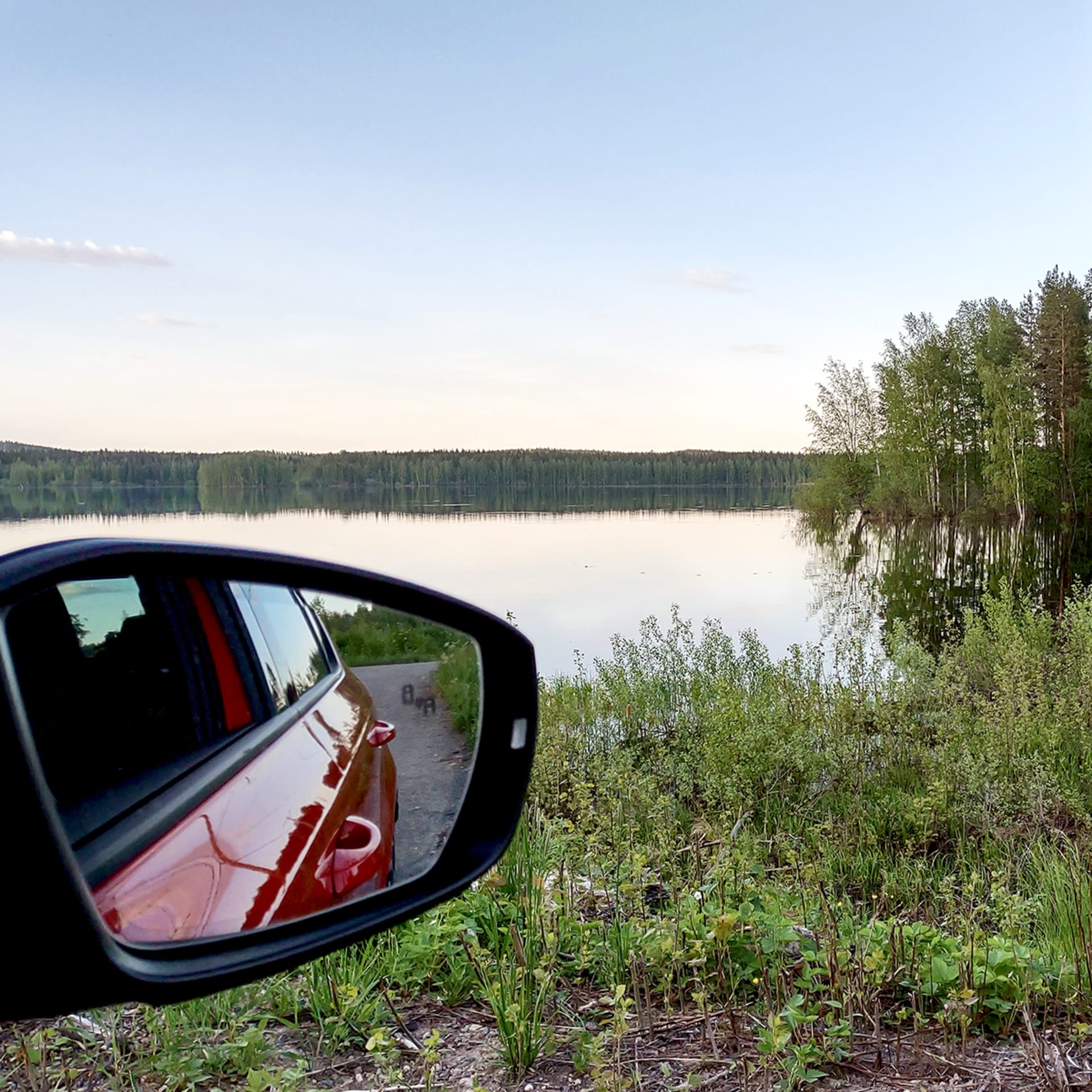 Car mirror by a lake in summer