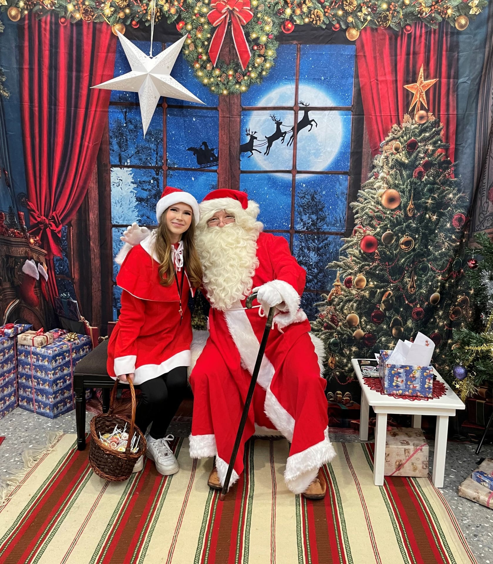 Joulupukki ja tonttu istuvat pukin tuvassa ja hymyilevät kameralle