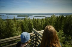 Two women in a lookout tower viewing a lake and forest landscape.