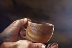 In the hands is a kuksa wooden cup with Ylläskammi engraved on it.