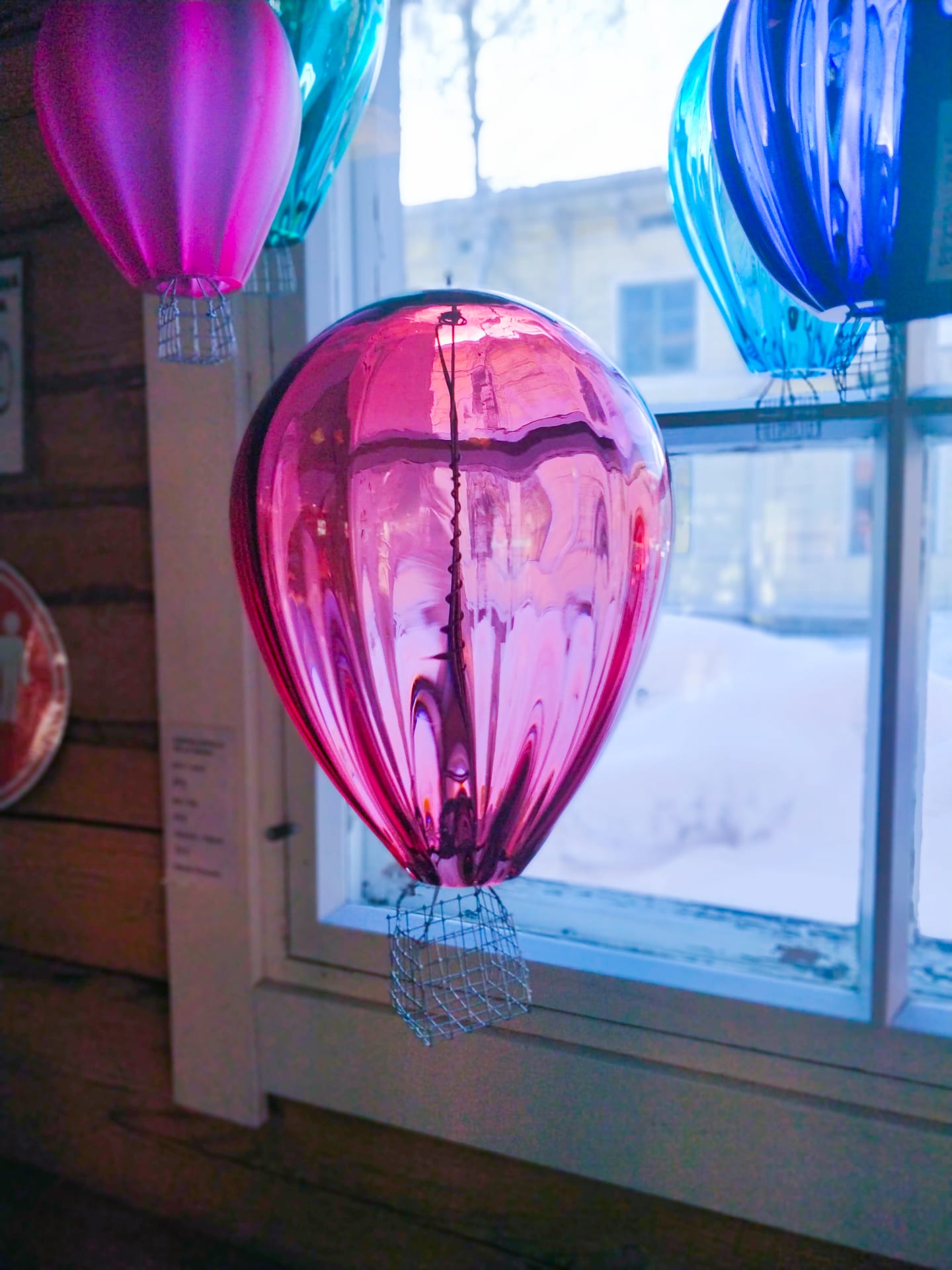 Kuvassa ikkunan edessä oleva lasitaideteos, vaaleanpunainen kuumailmapallo