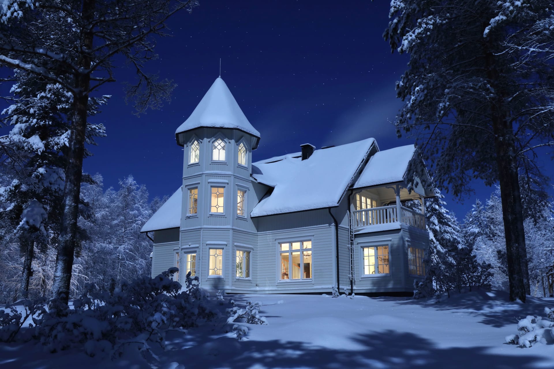 Snow-blanketed Villa Cone Beach stands within woods, illuminated by a full moon and stars, with warm indoor light filtering through windows into the bluish winter night.