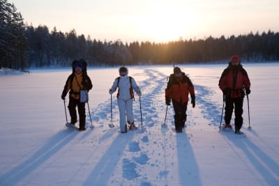 Four people snowshoeing on a lake in a cold winter day with light sunshine