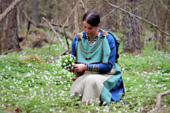 Euran emännän muinaispuku kuvattuna naisen yllä valkovuokkojen keskellä.