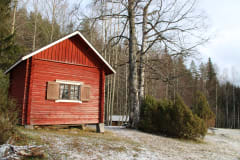 Hirsinen tupa talvisella pihamaalla. Maassa on vähän lunta, tuvan taustalla metsää. Kuva: Marjo Kämäräinen