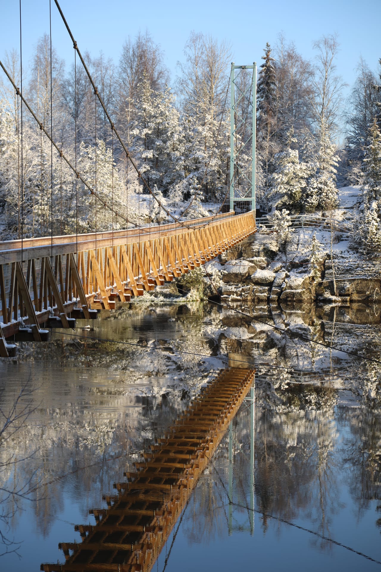Vanha riippusilta heijastuu talvisena päivänä vedenpinnasta.